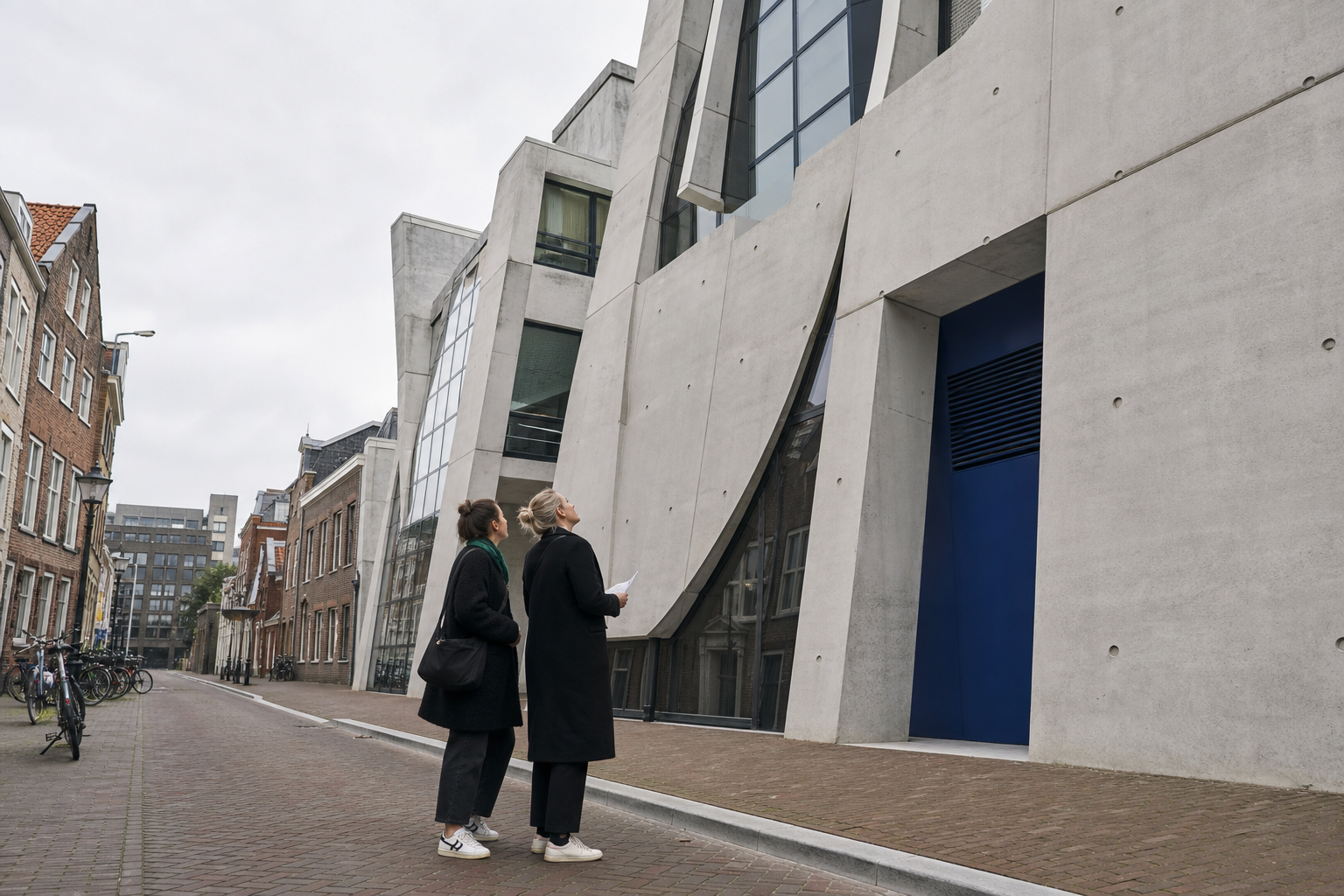 Twee wandelaars bekijken de schuine betonnen gevel van een modern gebouw in een Nederlandse straat